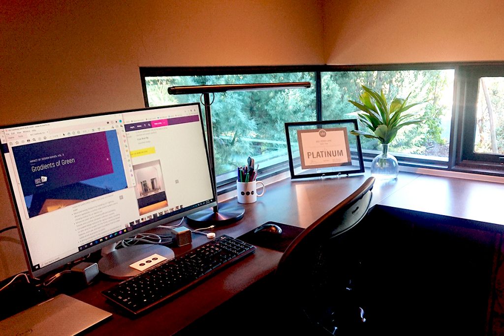 Home office with eye-level desk, windows and plants.