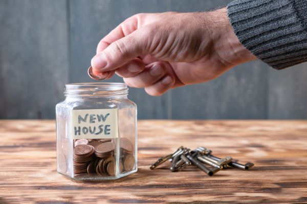 Man's hand add dimes to jar labelled New House